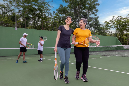 Cuatro personas, que usan ropa deportiva, están en medio de una cancha de tenis en donde cada uno sostiene una raqueta, mientras disfrutan de los espacios y los planes en el hotel Lagosol