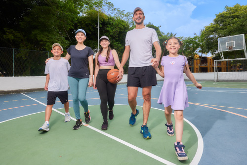 Familia de cinco personas, que usan ropa deportiva, van caminando por una cancha de básquet que está ubicada en el exterior de una de las locaciones donde se puede disfrutar de los mejores planes en el hotel Lagosol