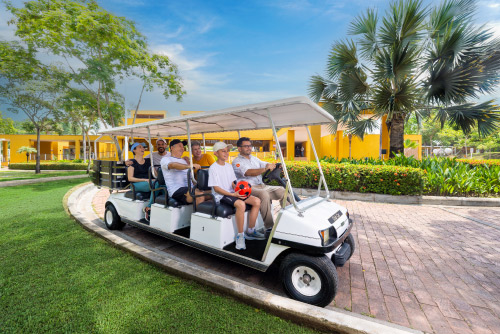 Seis personas están sobre un carro de golf de color blanco que avanza por un sendero rodeado de naturaleza que hace parte de la oferta de planes vacacionales en Lagosol