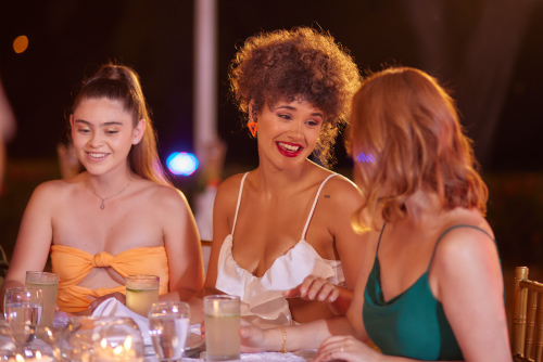 Tres mujeres, que usan vestidos de diferentes colores, están sentadas en medio de un restaurante elegante mientras disfrutan de uno de los planes vacacionales en Lagosol