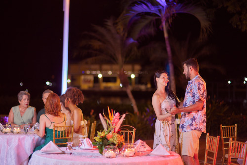 Pareja está mirándose fijamente a los ojos en un restaurante que tiene las mejores tarifas y planes del hotel Lagosol Compensar, en medio de una noche en un lugar con palmeras