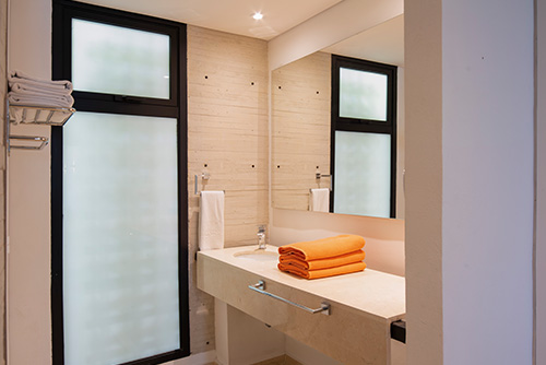 baño-del-hotel-lagomar​  Texto ALT:  Fotografía de Lagomar, un hotel en Girardot, que muestra el baño de las habitaciones en el que se ve el lavamanos, un espejo y tres toallas de color naranja