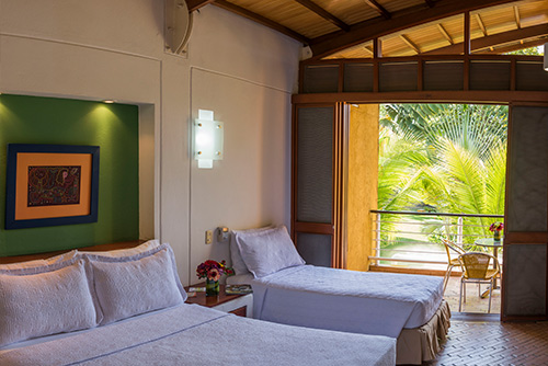 Fotografía del interior de las habitaciones en Lagosol, que muestra dos cama, una mesa de noche con un florero y un balcón con sillas
