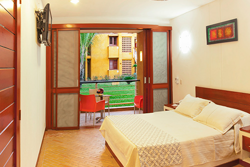 Habitación sencilla del hotel Lagosol Compensar, que muestra una cama doble, un televisor y un balcón con dos sillas rojas