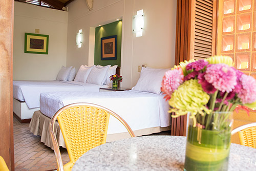 Toma de una habitación del hotel y Parque Acuático Lagosol, en la que se ven dos camas sencillas, una cama doble, una silla y un florero con flores amarillas y rosadas