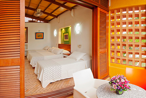 Fotografía de una de las habitaciones en hotel Lagosol de Compensar, que muestra dos camas sencillas, una cama doble, una silla blanca y una mesa en murano