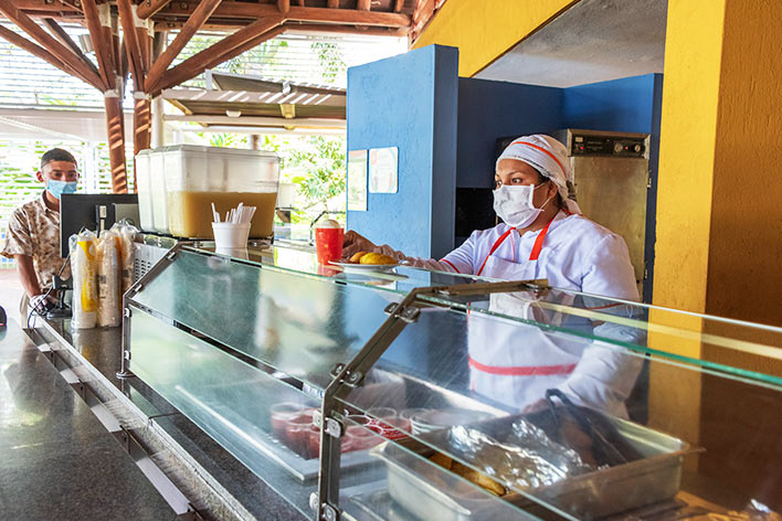 Mujer que viste ropa de chef, está en el restaurante de Lagosol Compensar sirviendo salpicón y empanadas