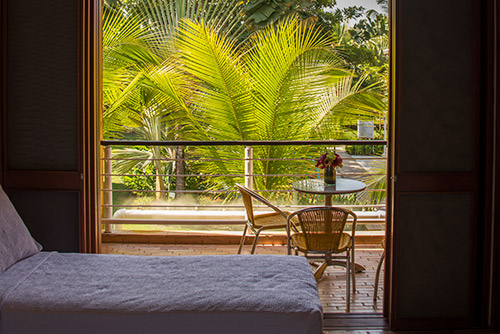 Imagen del balcón que tienen las habitaciones de Lagosol Compensar, en el que hay dos sillas de madera y una mesa con un florero