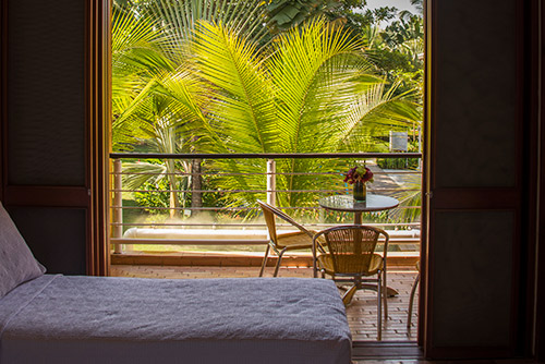 Fotografía de uno de los balcones que tienen algunas de las habitaciones de los planes en hotel Lagosol de Compensar, en el que hay dos sillas de madera y una mesa con un florero