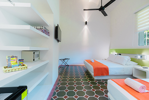 Habitación perteneciente a los descuentos especiales del centro vacacional Las Palmeras con dos camas dobles y mesas de noche para cada una, un televisor, un armario, un ventilador y una ventana