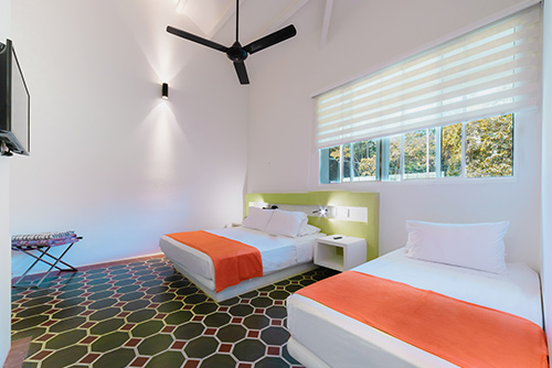 Habitación de Las Palmeras en Villeta perteneciente al plan básico para niños de 2 a 11 años, que cuenta con dos camas sencillas, un televisor, un ventilador y una ventana grande