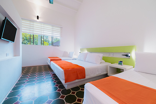 Habitación con descuento del hotel Las Palmeras con un piso de baldosas simétricas con tres camas, dos dobles y una personal, con una mesa de noche, un televisor y una ventana