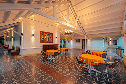 Restaurante del hotel Las Palmeras con un piso de baldosas verde oscuro y morado donde están ubicadas cuatro mesas con manteles naranjas y sillas negras