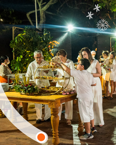 Personas, vestidas con prendas blancas, están haciendo fila en un buffet de fin de año, eligiendo su comida favorita para la noche
