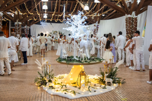 Buffet navideño, decorado con figuras blancas y luces amarillas, en donde se ven personas vestidas con color blanco haciendo fila para elegir sus alimentos favoritos​