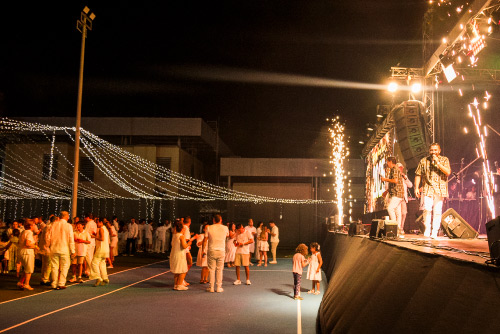 Escenario iluminado con músicos en vivo frente a un público vestido de blanco, disfrutando de un concierto como parte de la celebración en Lagomar