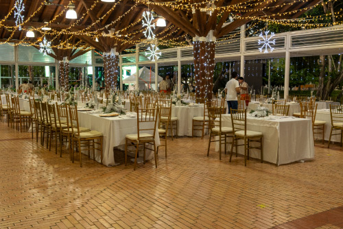Montaje de cena navideño, decorado con luces amarillas y blancas, con mesas y sillas distribuidas para las familias