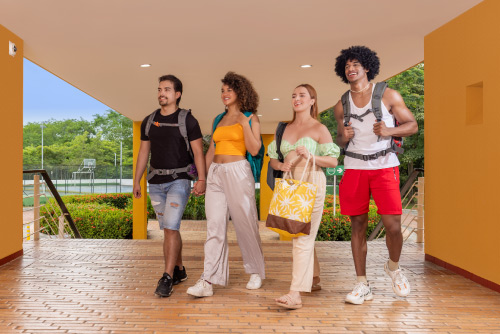 Cuatro personas jóvenes que usan ropa para clima cálido van caminando por un pasillo de paredes de color mostaza, el cual los lleva a las habitaciones en el hotel Lagosol