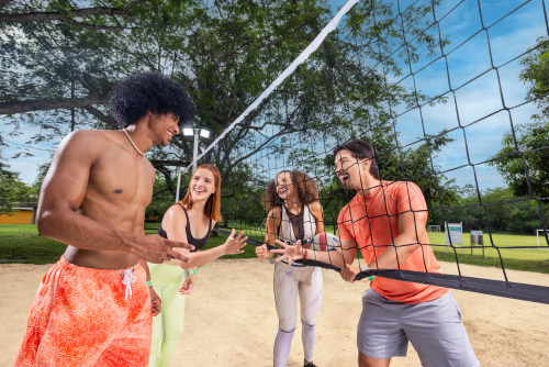 Dos hombres y dos mujeres que usan ropa para un clima cálido comparten en una cancha de vóley playa, en medio de un día soleado, en una de las locaciones disponibles en los planes turísticos de Lagosol