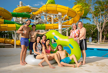 Fotografía de ocho personas, cuatro mujeres y cuatro hombres, en los toboganes del hotel y parque acuático Lagosol, están sonriendo con un flotador color verde en forma de ocho en sus manos
