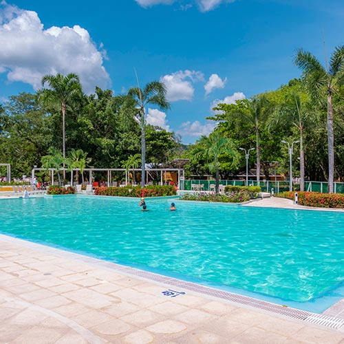 Piscina con agua cristalina y tres personas adentro compartiendo y disfrutando de las ofertas de alojamiento en el hotel Lagosol fin de semana festivo. Alrededor se ve gran cantidad de naturaleza, todo esto en medio de un día soleado
