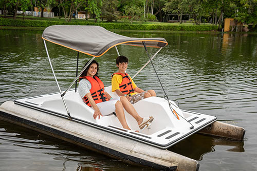 Pareja usando chalecos salvavidas, compartiendo en un bote con parasol y pedales, en medio del lago incluido con el plan fin de semana festivo Lagosol. Alrededor hay gran cantidad de vegetación