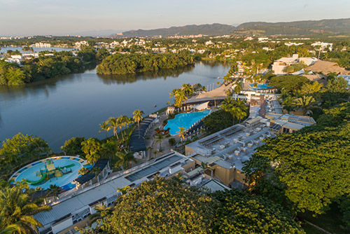 Toma aérea de un hotel que tiene tres piscinas y un gran lago. Alrededor se ven gran cantidad de árboles y los edificios de las instalaciones del lugar en donde se puede acceder al paquete turístico con descuento para Lagosol