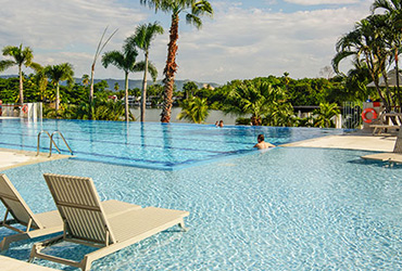 Imagen de la piscina del hotel Lagomar Compensar,  en la que se ve una piscina honda y una de poca profundidad, a su alrededor hay sillas de playa y zonas verdes