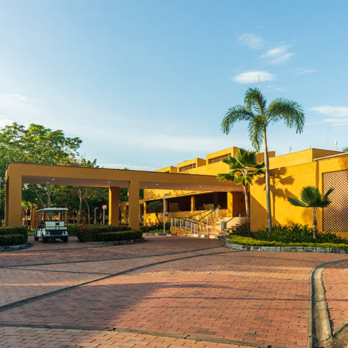 Instalaciones de Lagosol en temporada baja, hay un edificio amarillo durante un día soleado, rodeado de palmeras y un carrito de golf estacionado a un costado