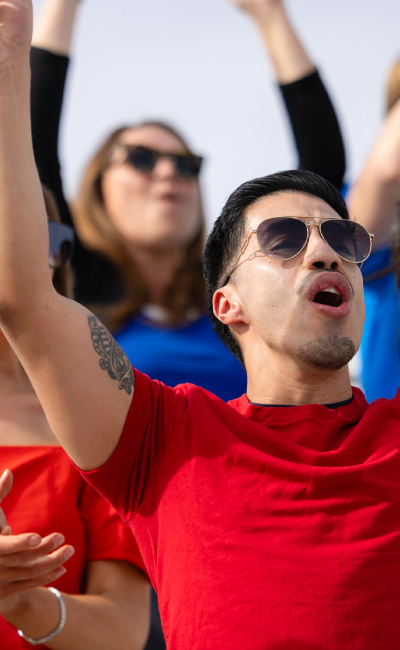 Un grupo de personas con camisetas rojas y gafas de sol celebra desde las gradas, disfrutando el ambiente lleno de emoción que se vive durante el viaje para el gran premio de Barcelona, mientras animan a los pilotos en plena competencia