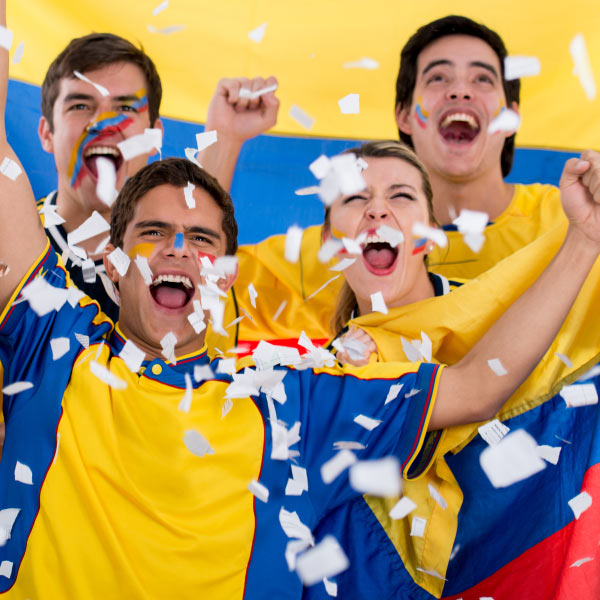 Cuatro personas que usan camisetas de Colombia, de color amarillo, azul y rojo, acompañados de una bandera de los mismos colores, celebran con sonrisas y alegría durante uno de los planes de turismo deportivo de Compensar