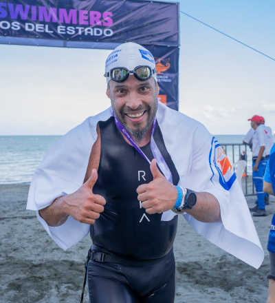 Hombre que usa traje de baño y gafas negras, sostiene una bandera de color blanco en la playa, luego de acceder a las mejores ofertas de turismo deportivo