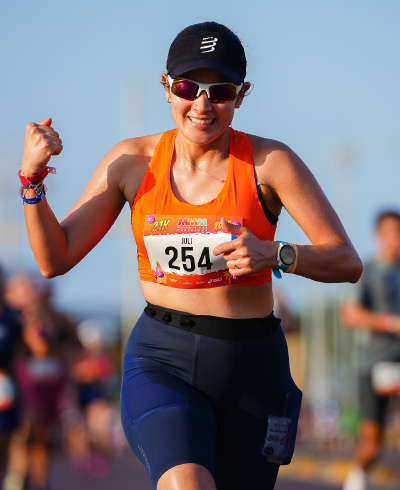 Mujer, con ropa para running de color azul y naranja, está corriendo en una competencia atlética, celebrando que llegó a la meta de la Media Maratón del Mar