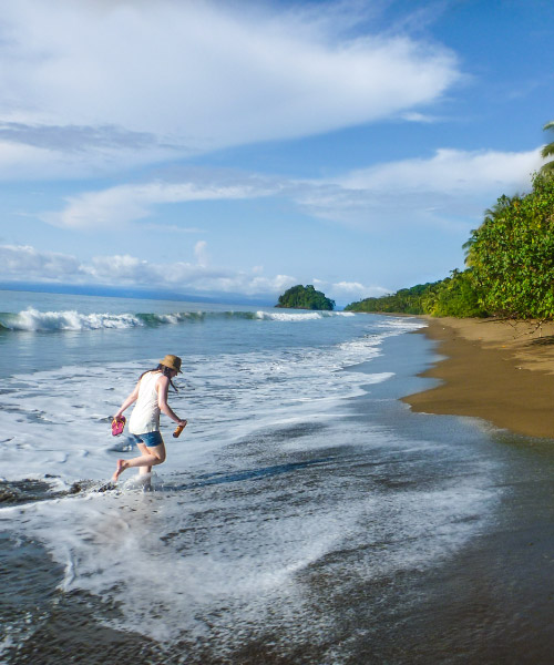 Mujer, que camina por la playa, es alcanzada por una ola del mar de Bahía Solano, luego de acceder a los mejores planes de turismo ecológico en Colombia