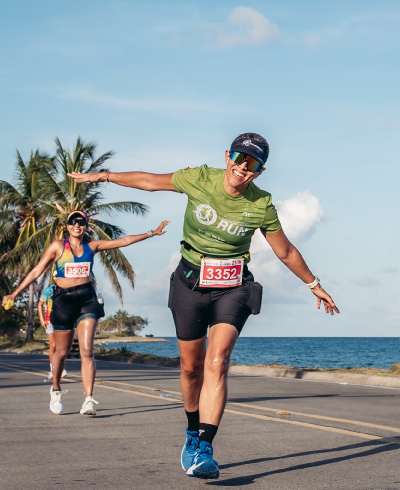 Mujer, vestida con prendas de color verde y negro, extendiendo sus brazos y celebrando haber terminado la maratón del plan turístico vuelta atlética San Andrés.​