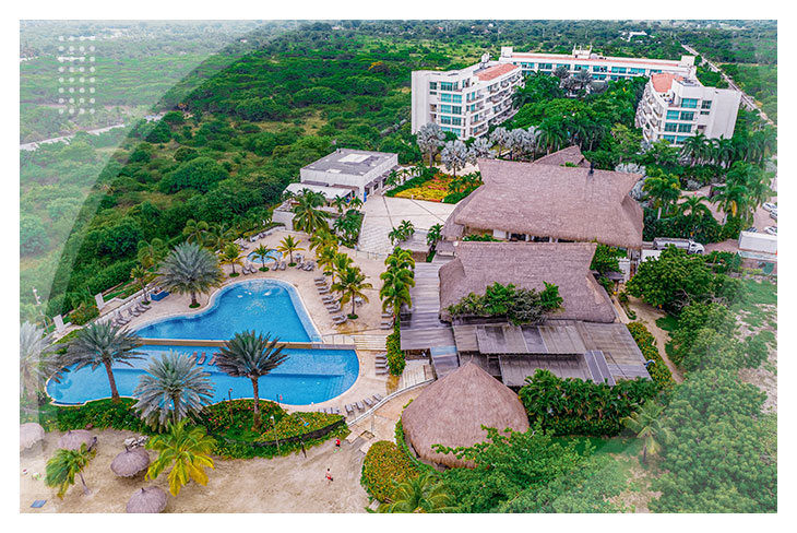 Vista aérea de un hotel rodeado de árboles con piscina azul, palmeras y techos en palma, una opción perfecta entre los mejores hoteles para hacer reservas en Cartagena.