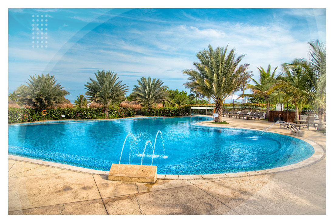 Piscina grande con chorros de agua, rodeada de palmeras bajo un cielo azul, perfecta para disfrutar en hoteles cerca a la playa Manzanillo.