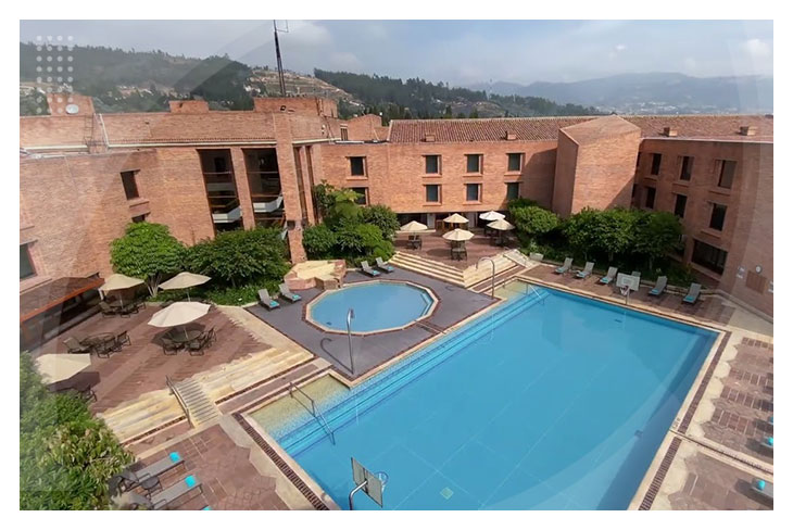 Piscina amplia con jacuzzi rodeada de sillas asoleadoras y sombrillas en un entorno natural con montañas de fondo en el Hotel Estelar Paipa.