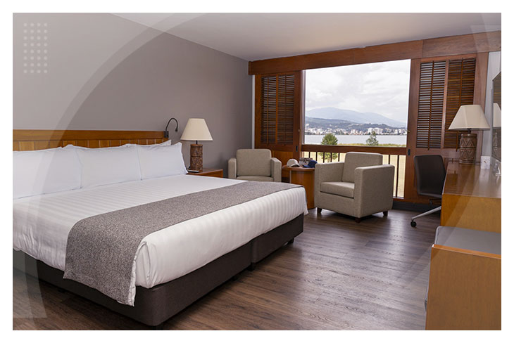 Habitación amplia con cama doble, escritorio, sillones y gran ventanal con vista natural en los hoteles de Paipa con descuento.