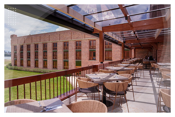 Zona de restaurante con techo de vidrio, múltiples mesas en una terraza con vista a zonas verdes en los hospedajes en Paipa al mejor precio.