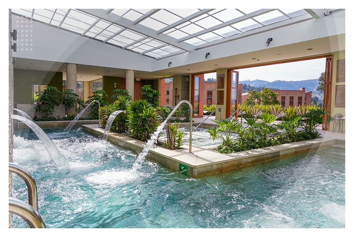 Zona de hidroterapia con caídas de agua y vegetación natural dentro de una piscina techada con vista a un paisaje montañoso en uno de los mejores hoteles en Boyacá.