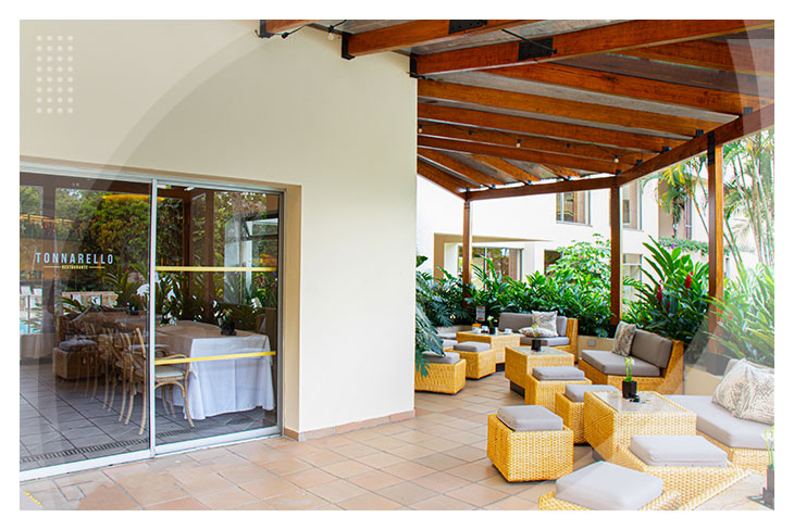 Zona de descanso al aire libre con sillas de mimbre y cojines claros, bajo techo de madera y rodeado de naturaleza tropical