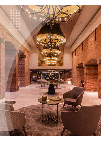 Lobby con sofás modernos, un par de mesas y decoración acogedora, rodeado de columnas y arcos de ladrillo, con grandes lámparas que iluminan este espacio en uno de los mejores hoteles de Bogotá.