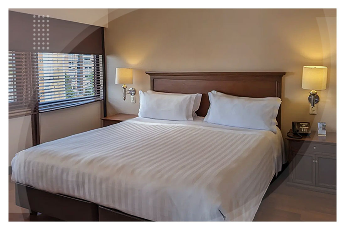 Habitación con cama amplia y sábanas blancas, ambientada con luz cálida, un par de mesas de noche, lámparas modernas y ventana con vista a la ciudad, ideal para quienes buscan promociones para reservar en el Hotel La Fontana.