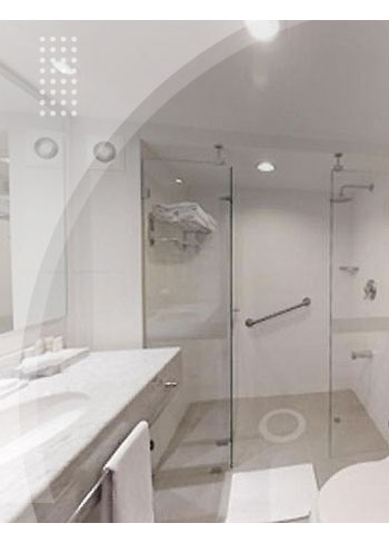 Baño moderno con ducha en vidrio, lavamanos amplio, inodoro y acabados blancos, en una de las habitaciones a las cuales se puede acceder con reservas en el hotel La Fontana a bajo precio.