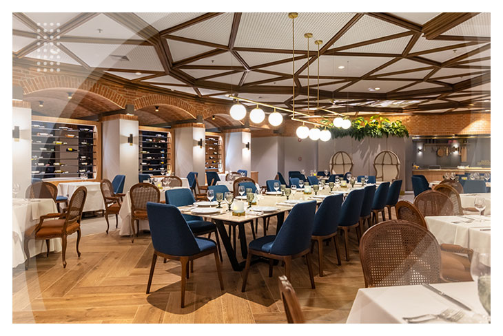 Restaurante elegante con varias mesas, sillas azules y marrones, iluminación cálida y techo de madera, en uno de los espacios que hacen parte de los restaurantes del Hotel La Fontana.