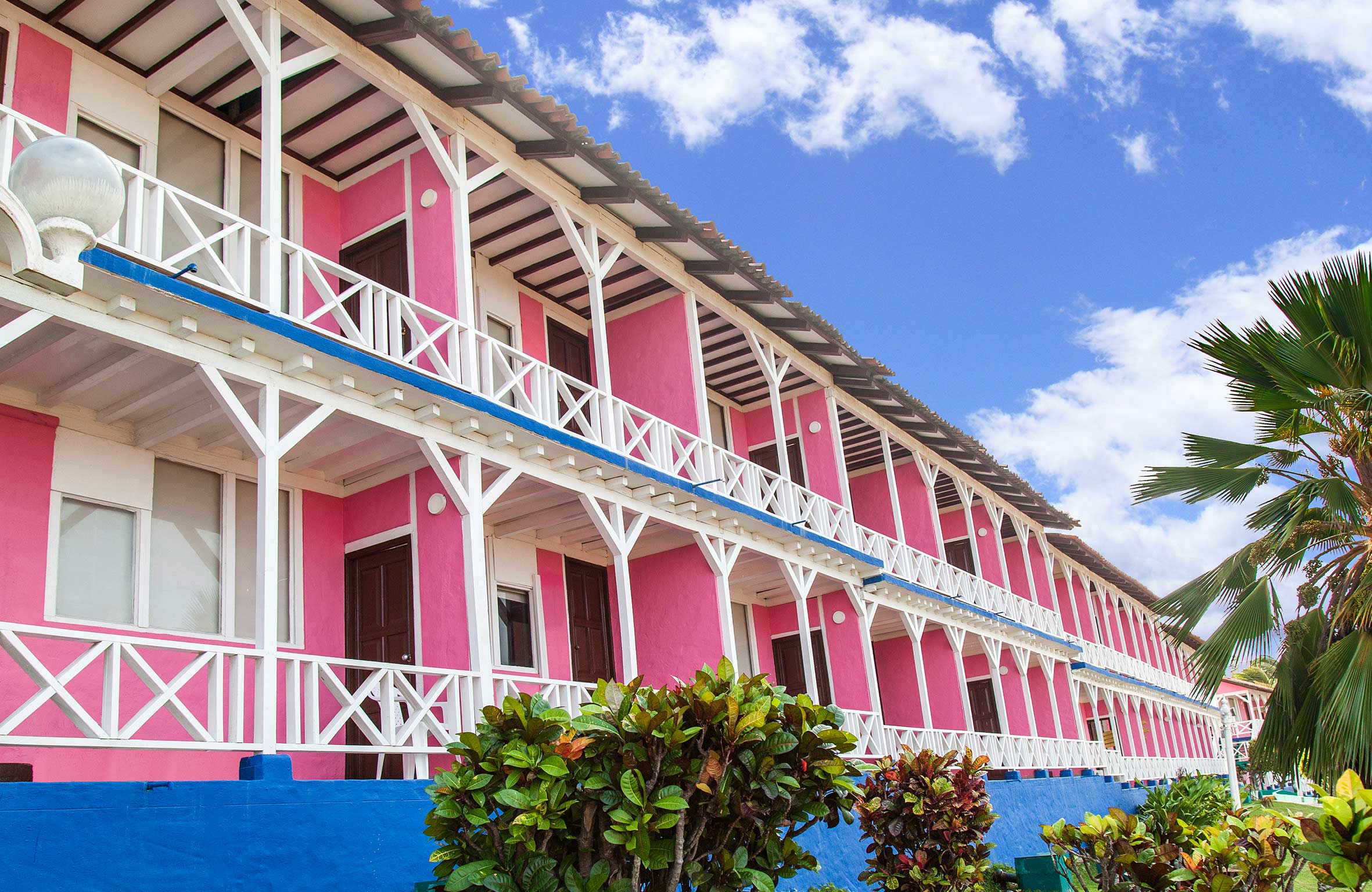 Fachada color rosado de un hotel incluido dentro de las promociones Hoteles Sol Caribe y Compensar, con balcones blancos y zonas verdes alrededor