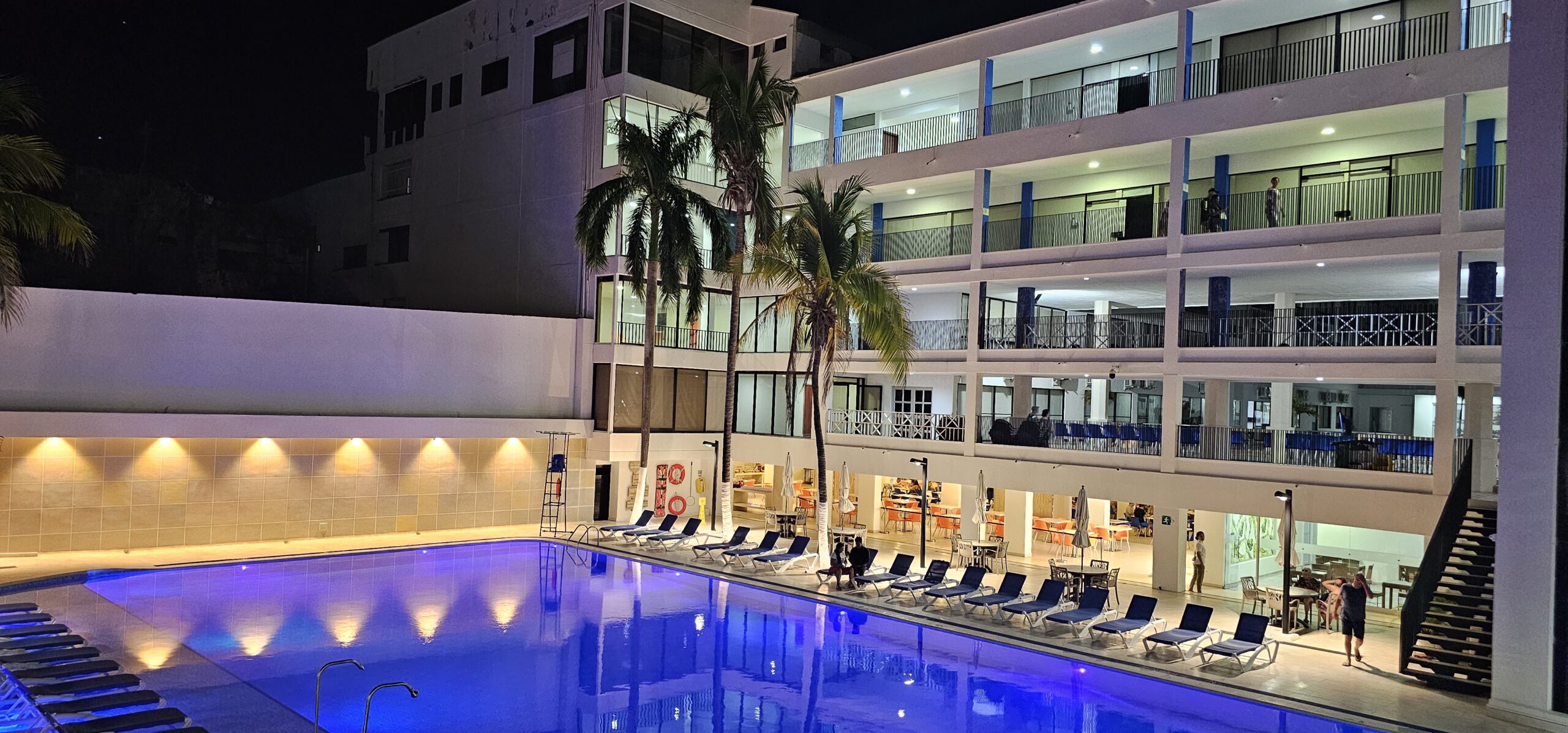 Piscina iluminada durante la noche, rodeada de sillas asoleadoras y palmeras dentro del hotel, una opción atractiva incluida en las ofertas de hoteles Sol Caribe para estancias nocturnas