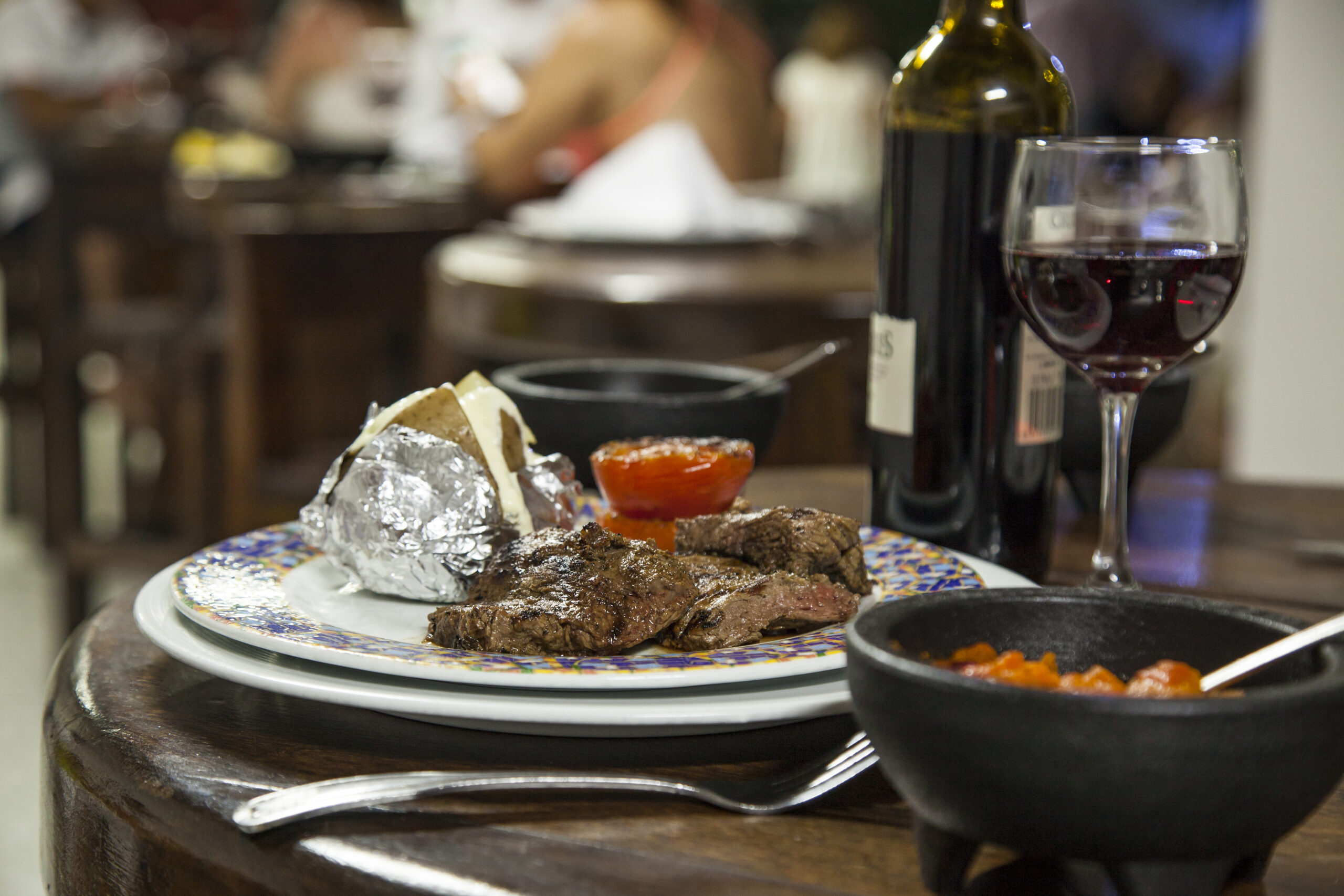 Plato de carne asada acompañado de guarniciones y una copa de vino sobre una mesa de madera, servido en el restaurante del hotel como parte de los paquetes de viaje a San Andrés Compensar
