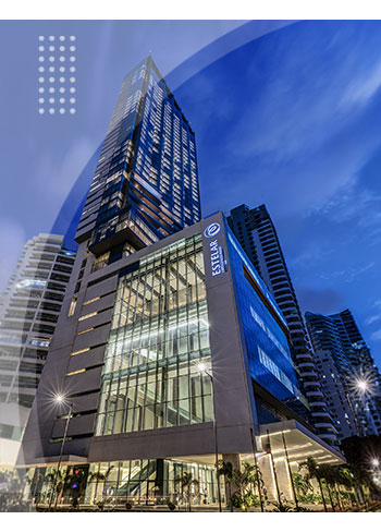 Edificio moderno con fachada de vidrio e iluminación nocturna, rodeado de rascacielos y palmeras, que hace parte del Hotel y centro de convenciones Estelar Cartagena.